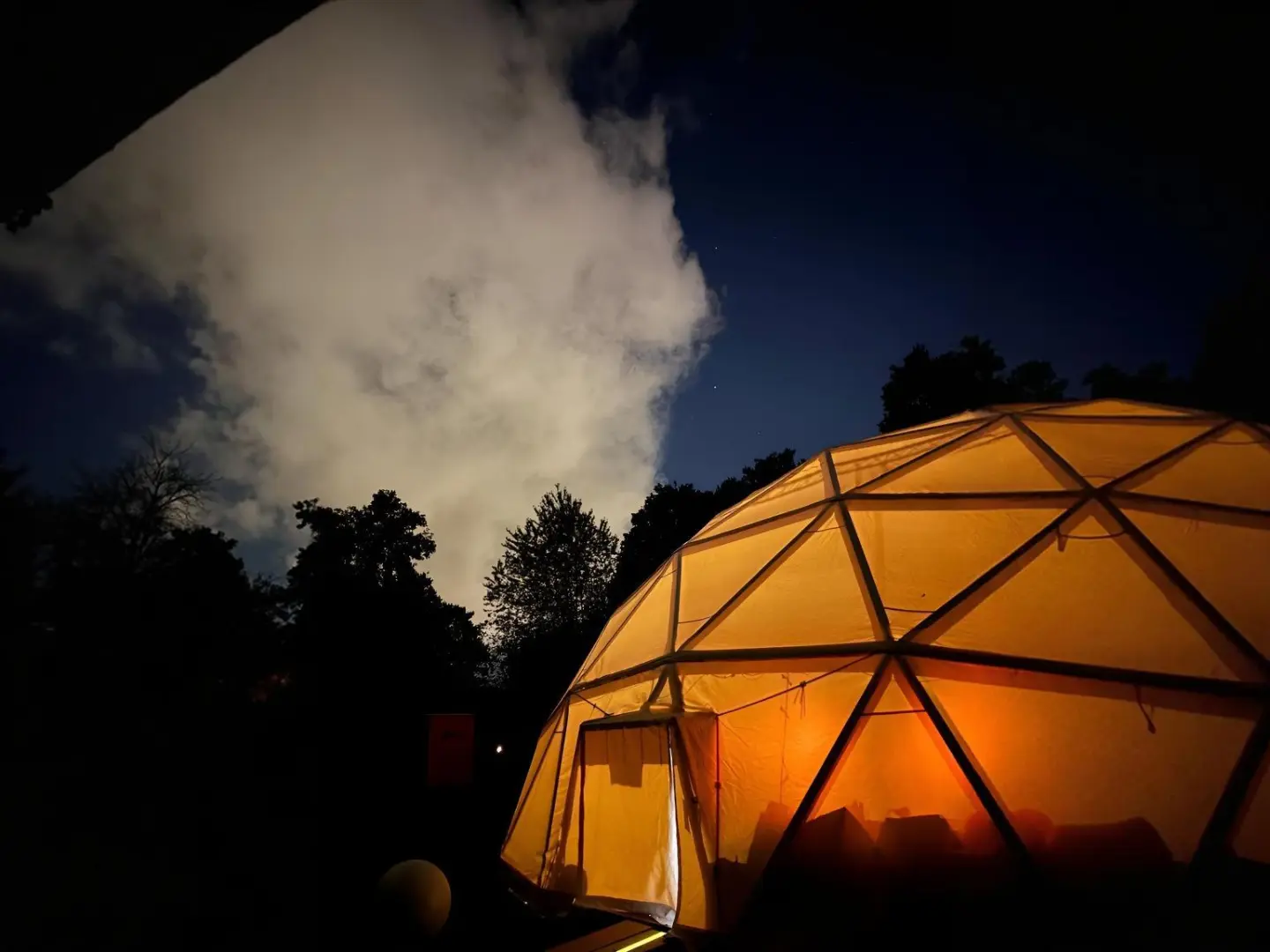 The illuminated dome at dusk between dark trees, a cloud drifting overhead
