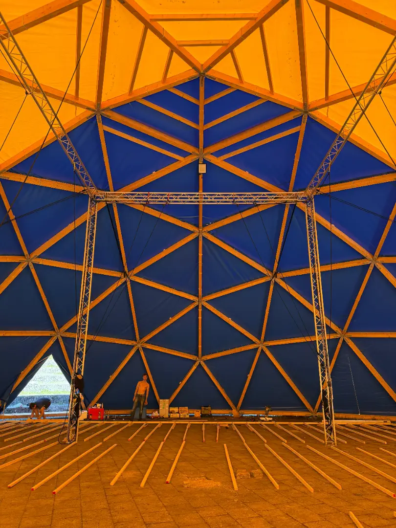 View up into the dome: the triangular wooden framework against a yellow and orange canopy