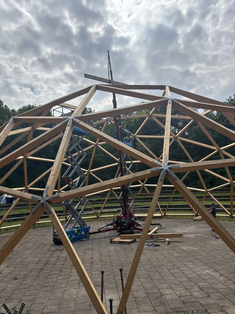 The dome frame under an overcast sky, a person in a purple jacket sitting at its base