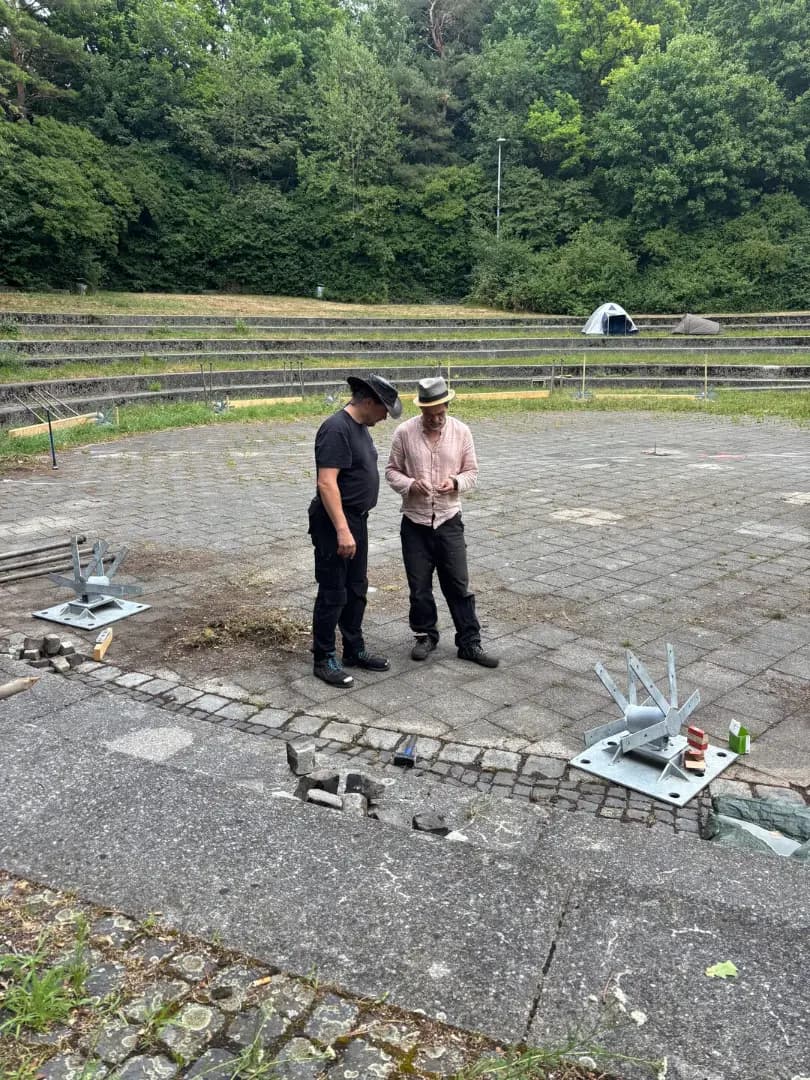 Two people standing in the empty Theatron discussing the parts laid out on the ground