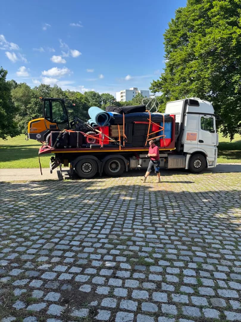 A loaded flatbed truck with material and frame parts on the paved area by the Ostpark