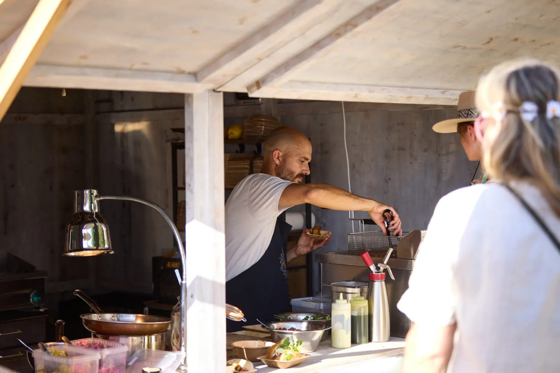 A cook plating a dish in the open kitchen while a visitor waits at the counter