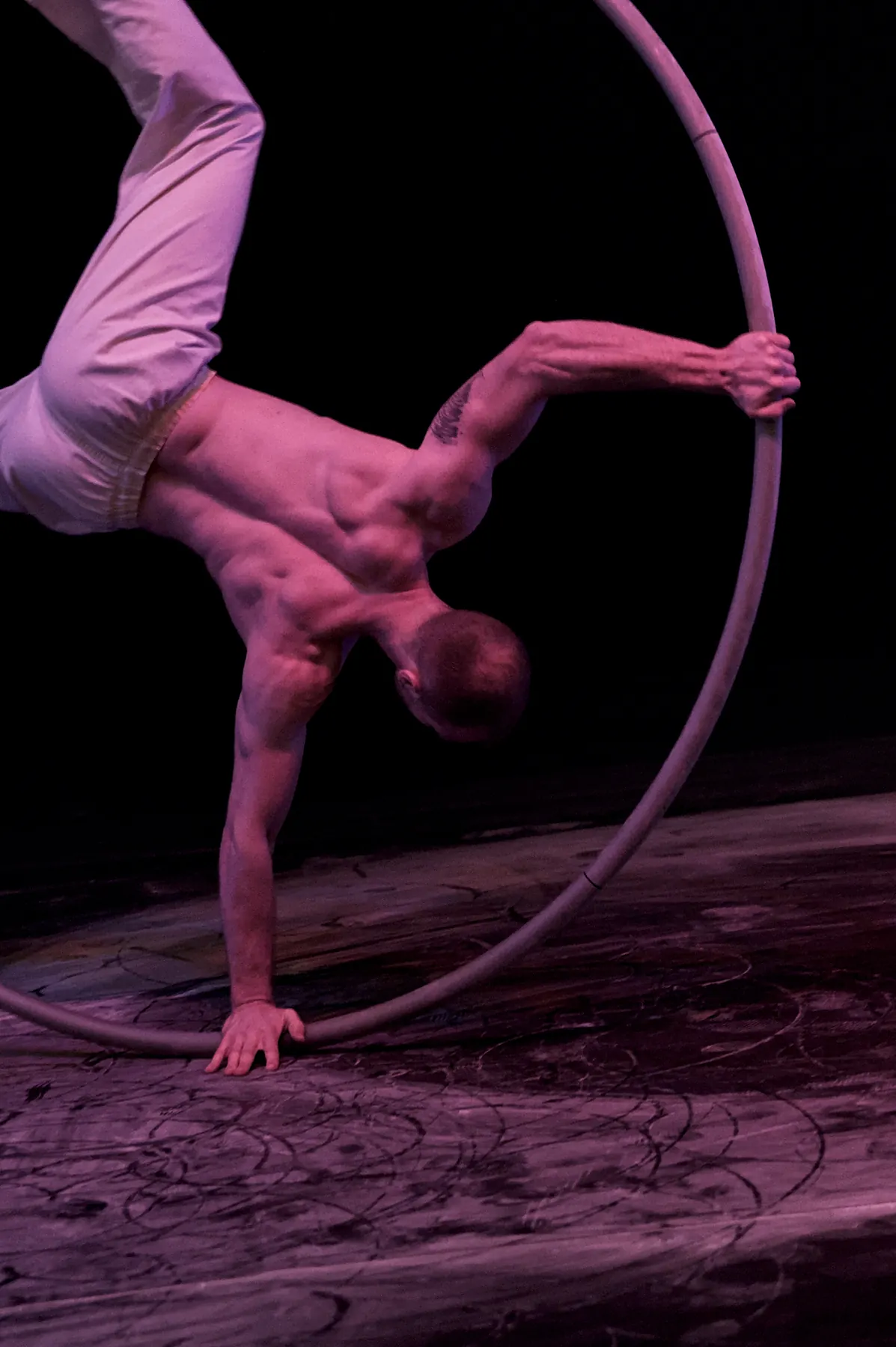Artist supporting himself on one arm inside a Cyr wheel with his legs stretched upward