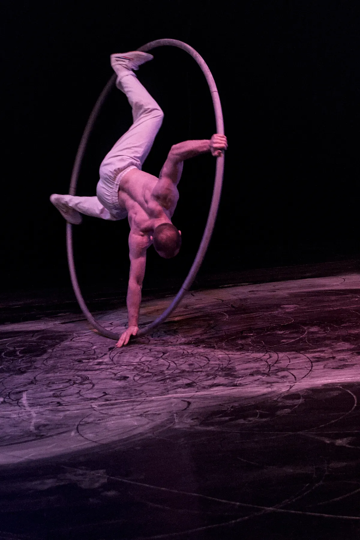 Artist in a handstand inside a Cyr wheel, the hoop tilted above a purple lit stage floor