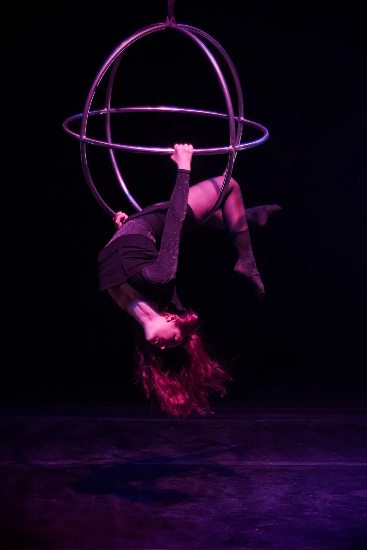 Artist hanging upside down in an aerial apparatus of two crossed hoops, long hair falling downward