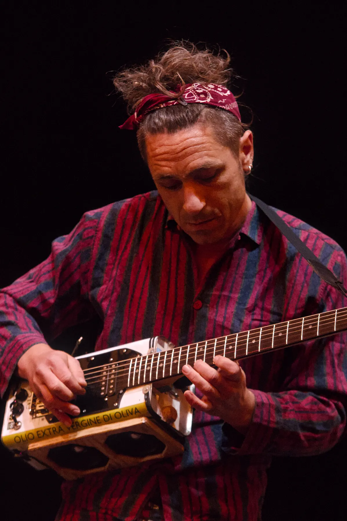 Musician wearing a headscarf playing a homemade guitar built from an olive oil tin