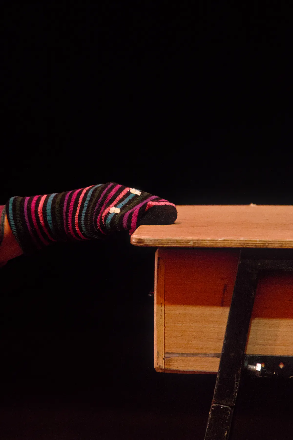Two legs in brightly striped legwarmers resting on the edge of a table, the rest of the stage dark