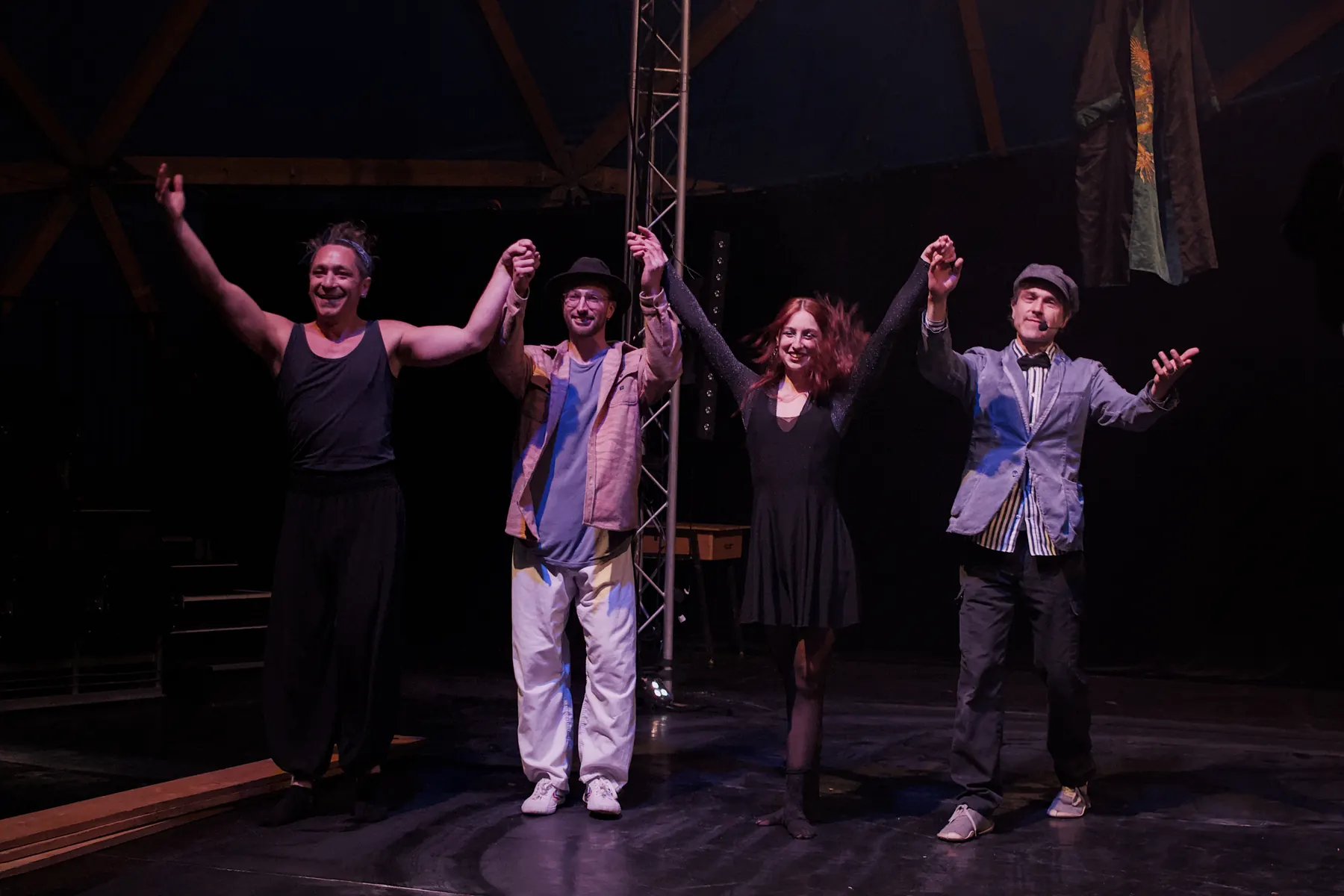 Four performers standing side by side for the final applause with their hands raised