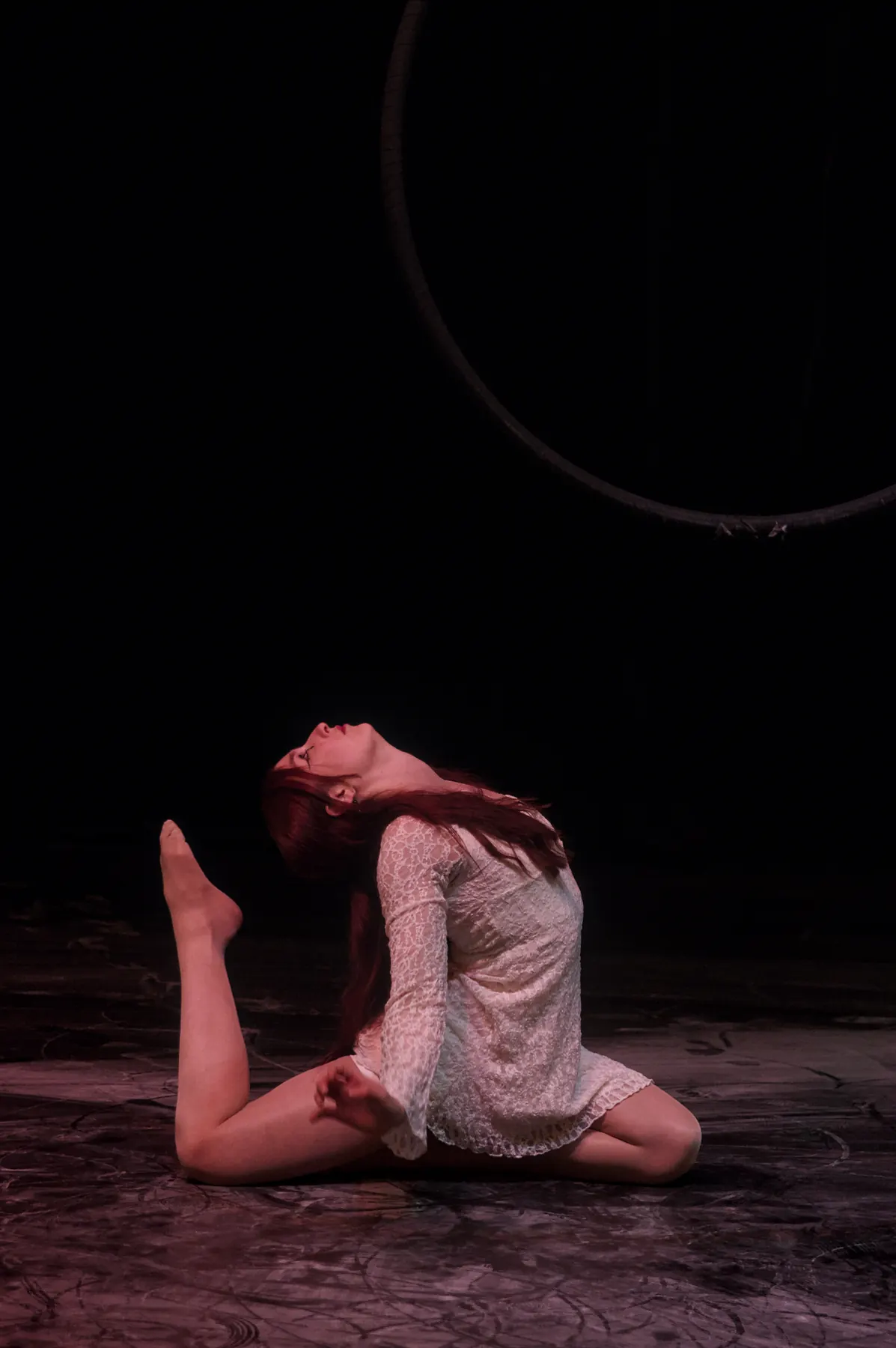 Dancer in a pale dress kneeling on stage, bending far backwards