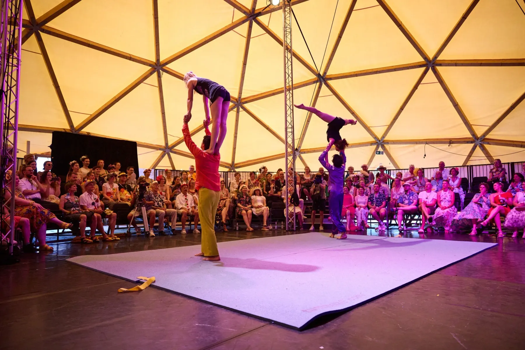 Partner acrobatics on a pale dance floor under the dome, the audience seated close all around
