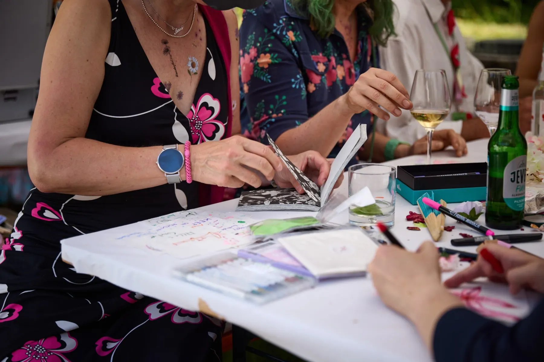 Several guests making things at a long table with paper, pens and wine glasses