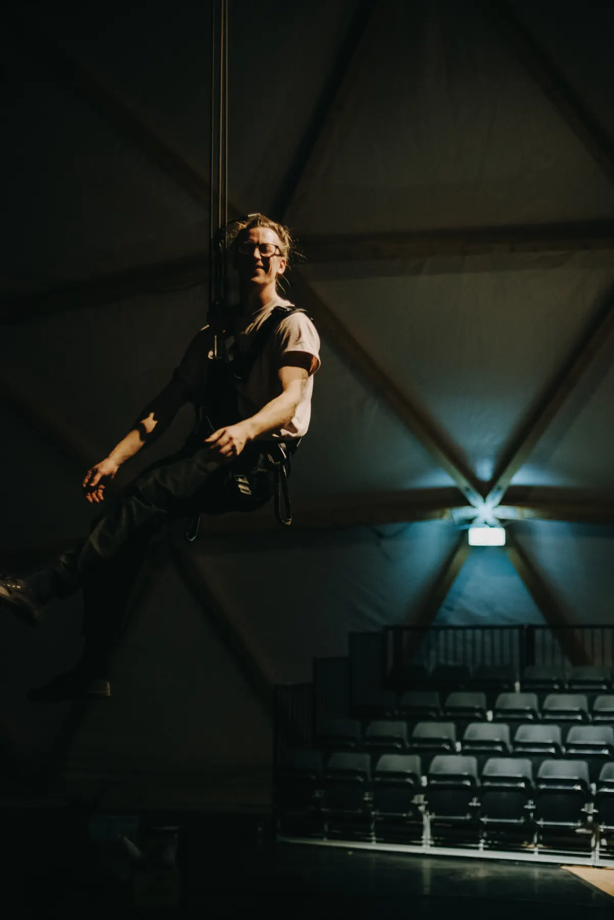 Artist sitting in a harness on a rope in front of the dome frame, the empty rows of seats below