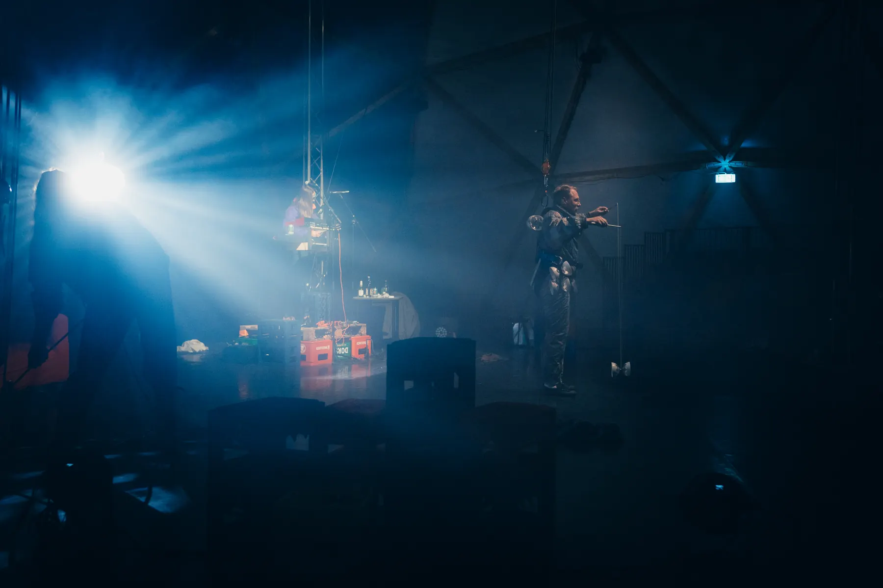 Blue spotlight beams cutting through haze above the stage, a musician standing to the right