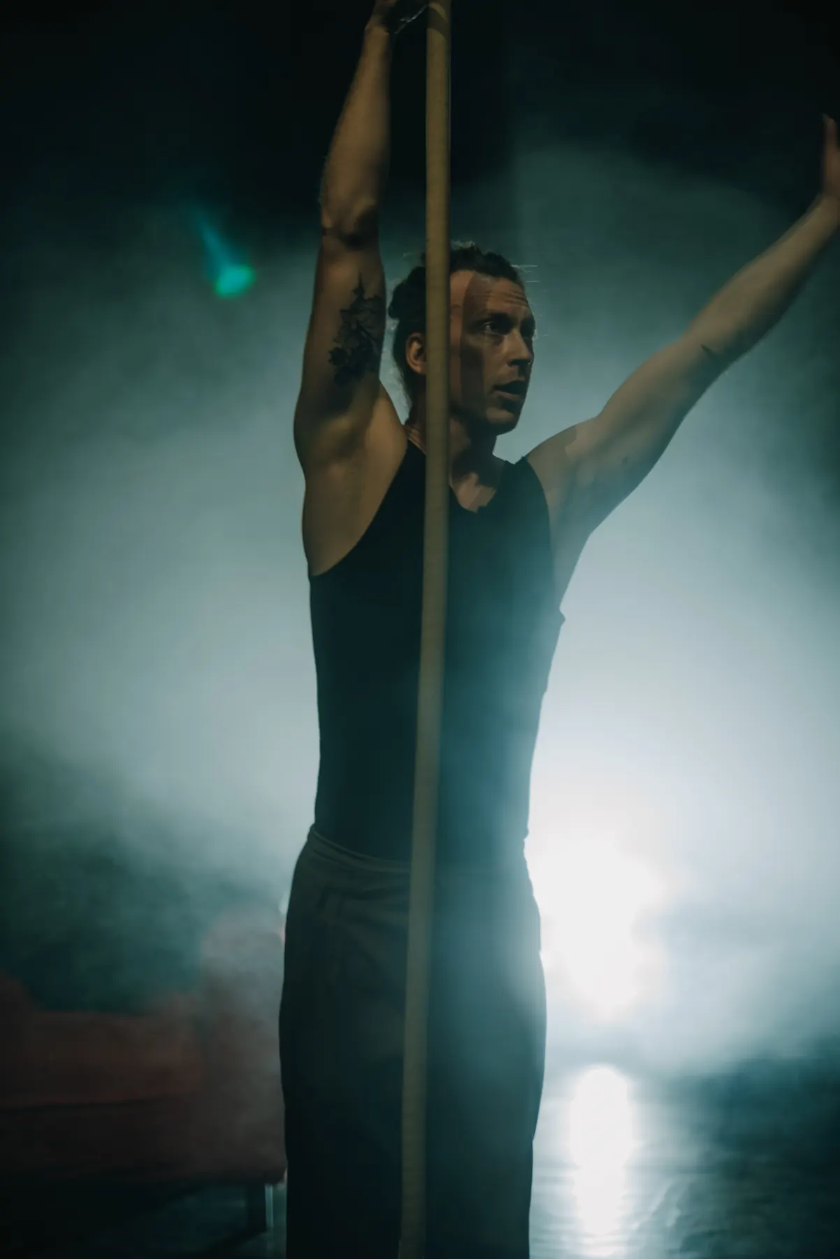 Artist reaching up along a vertical pole, green lit haze behind him