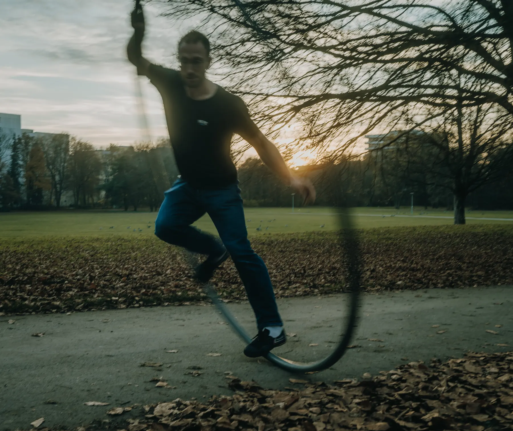 Artist spinning a Cyr wheel on a path in the park, the sun setting over the meadow behind