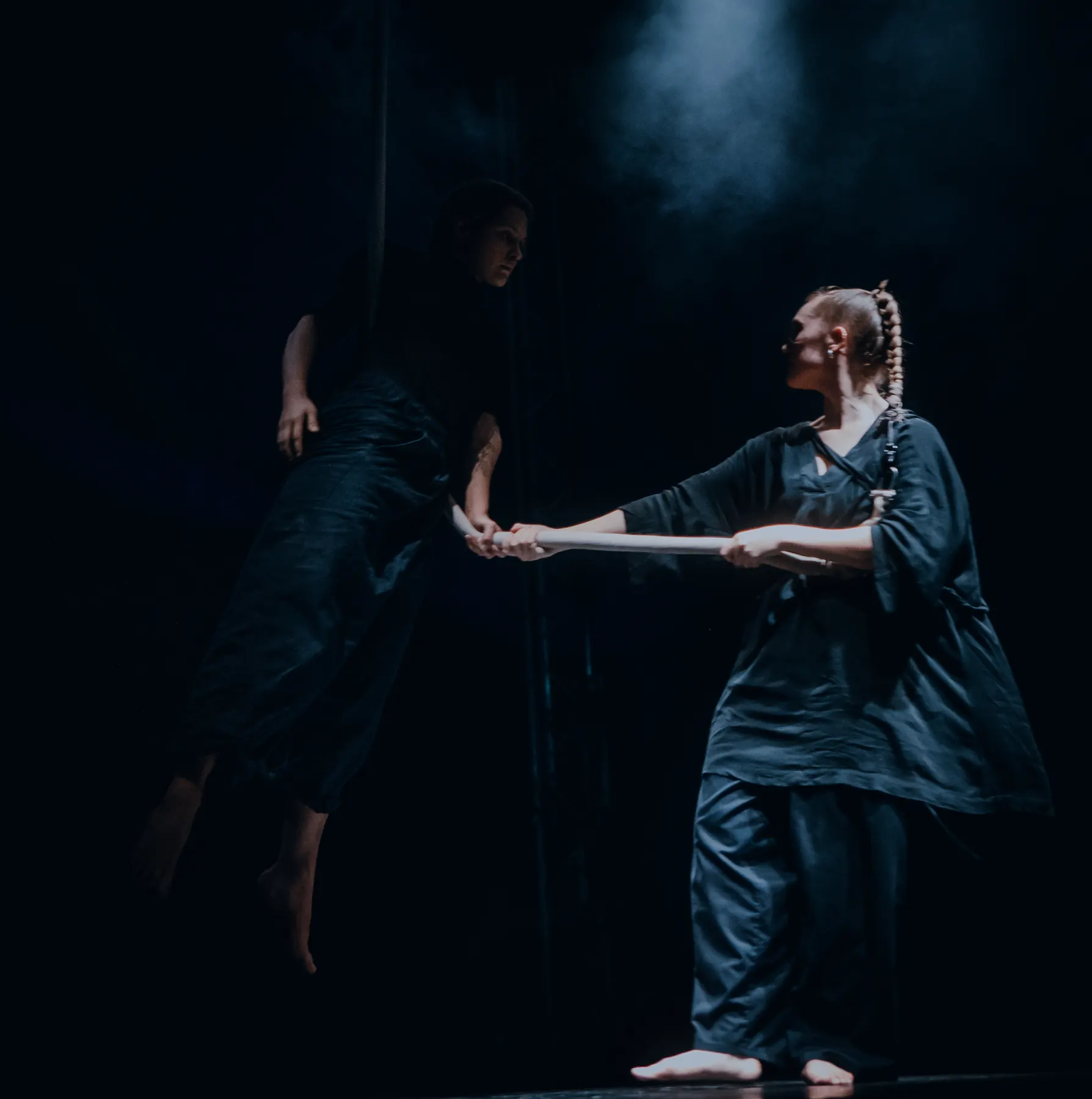 Two artists in a duo: one floating horizontally on a rope while the other holds both her hands