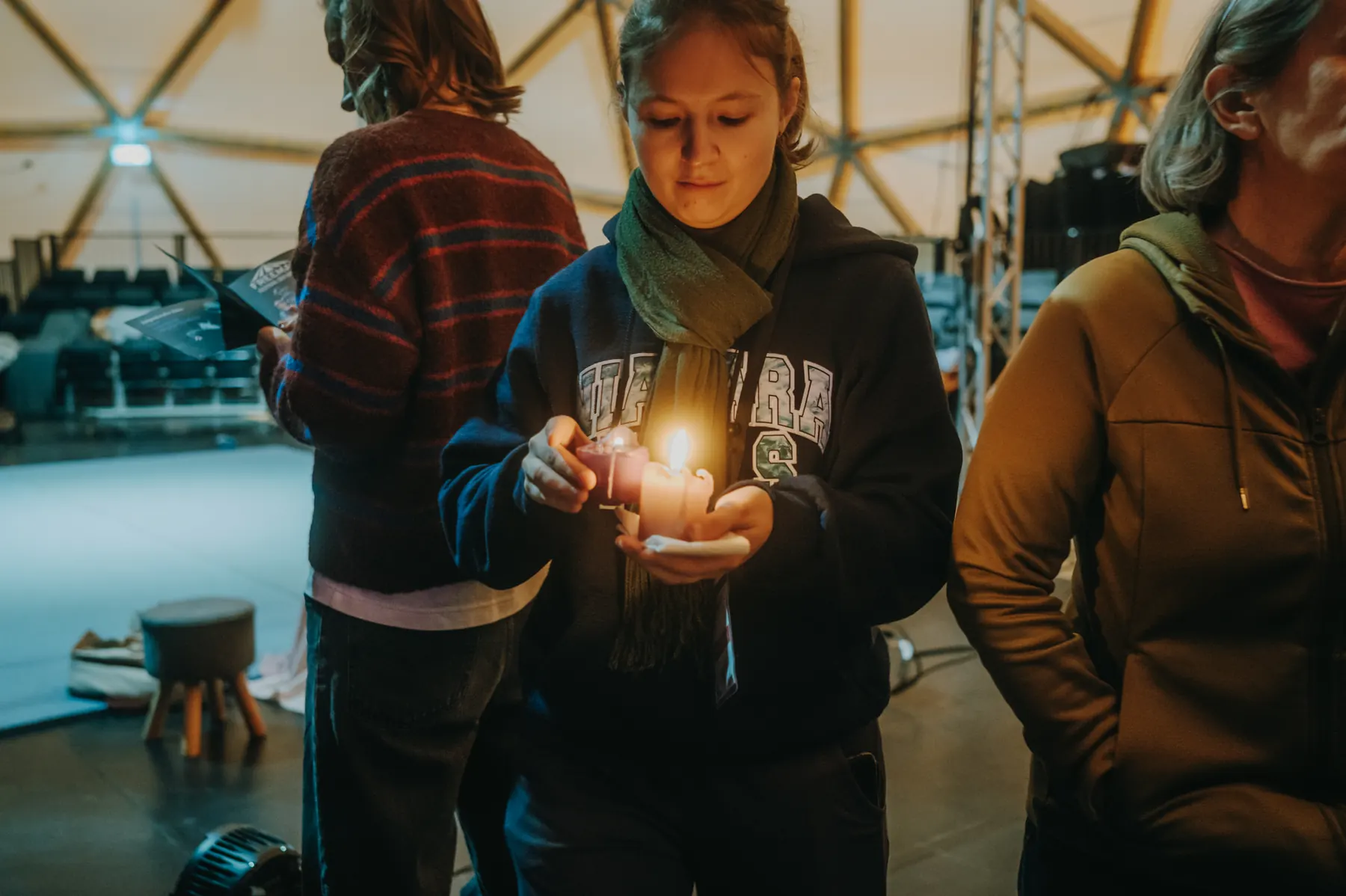 A young woman holding a lit candle in both hands, other guests standing around her