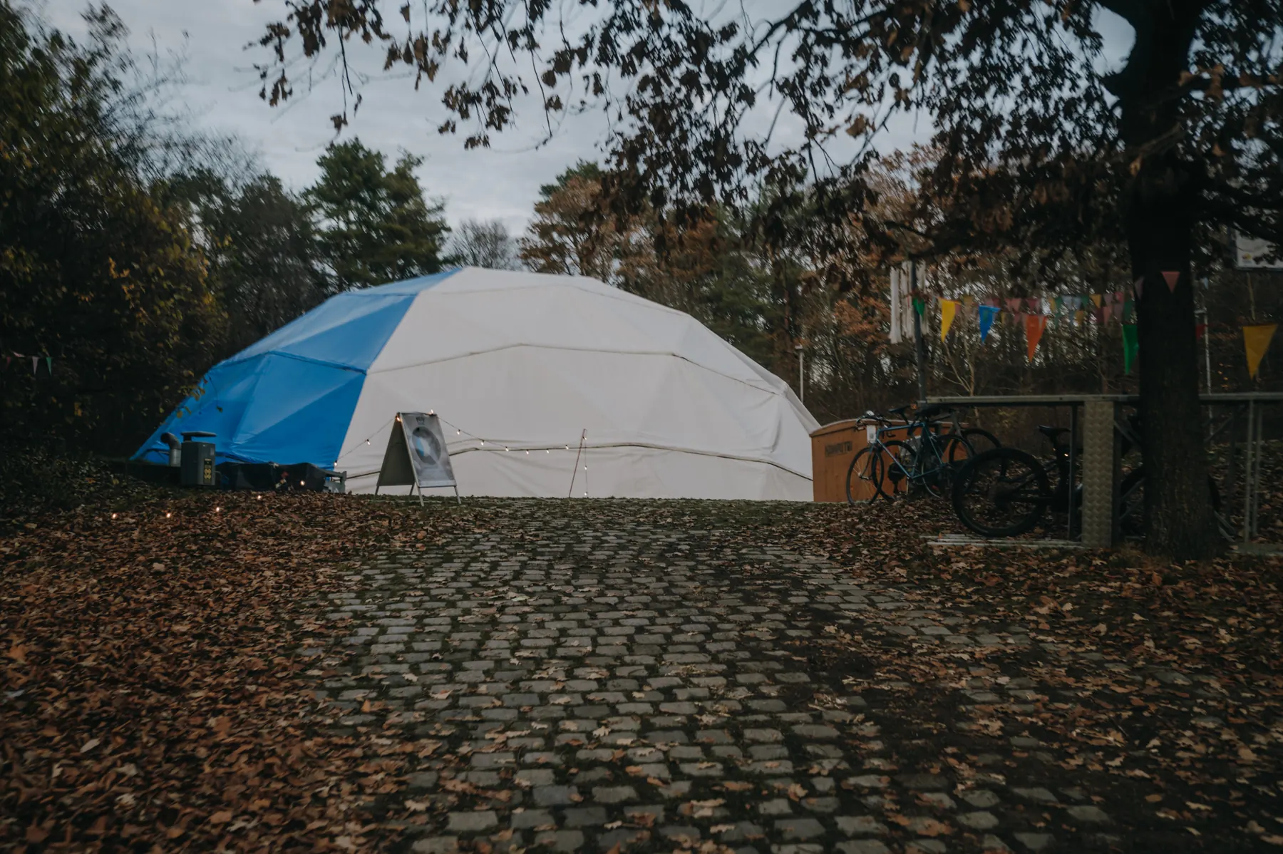 The white and blue dome in the park behind a path covered in autumn leaves, bunting strung between the trees