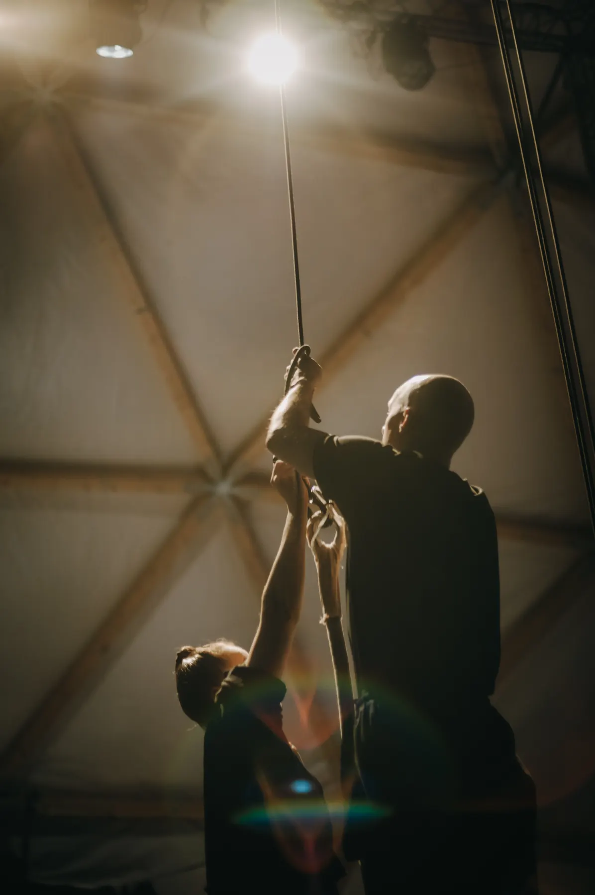 Two people rigging a rope into the apex of the dome, seen against the light