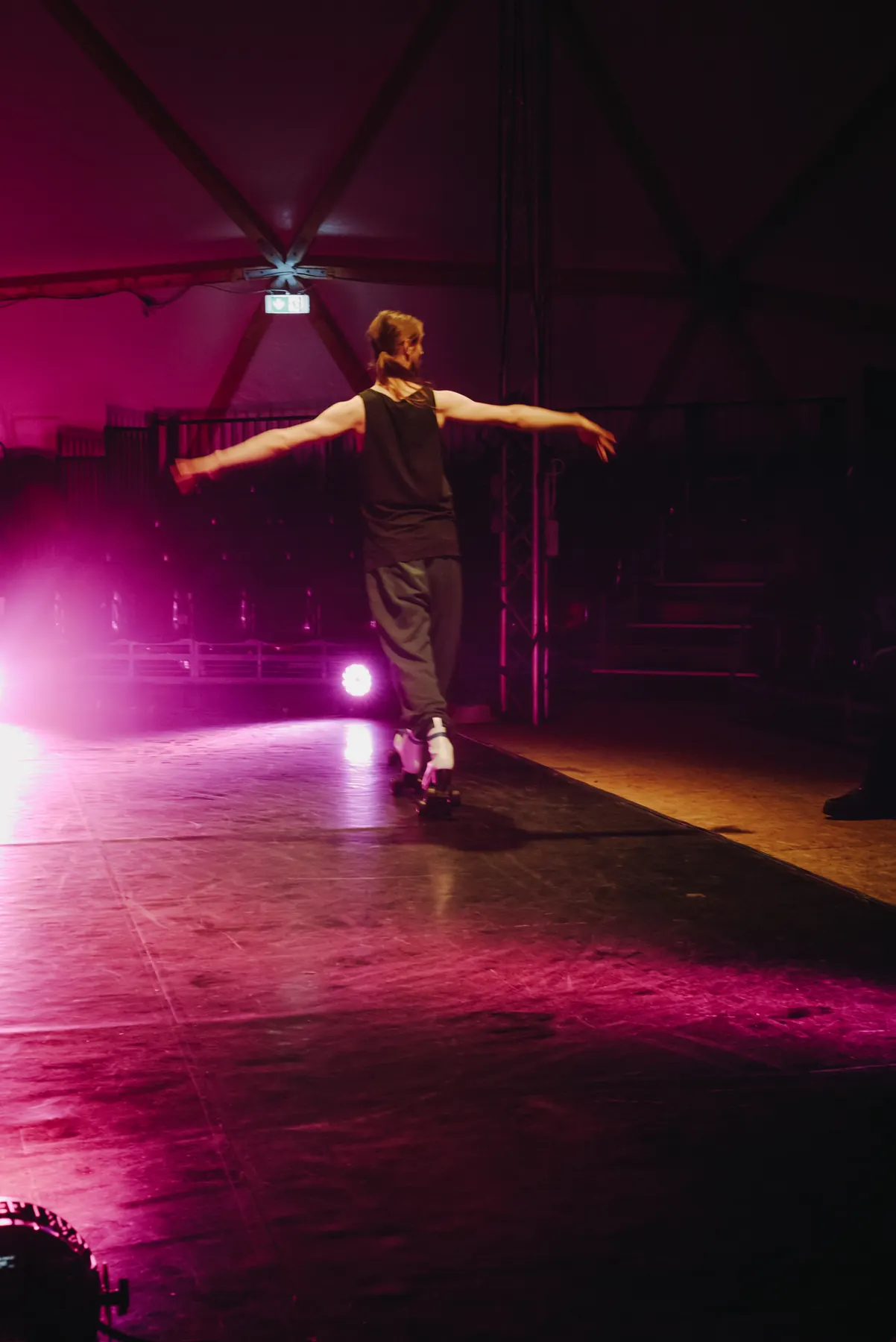 Artist on roller skates gliding through magenta light with arms spread wide