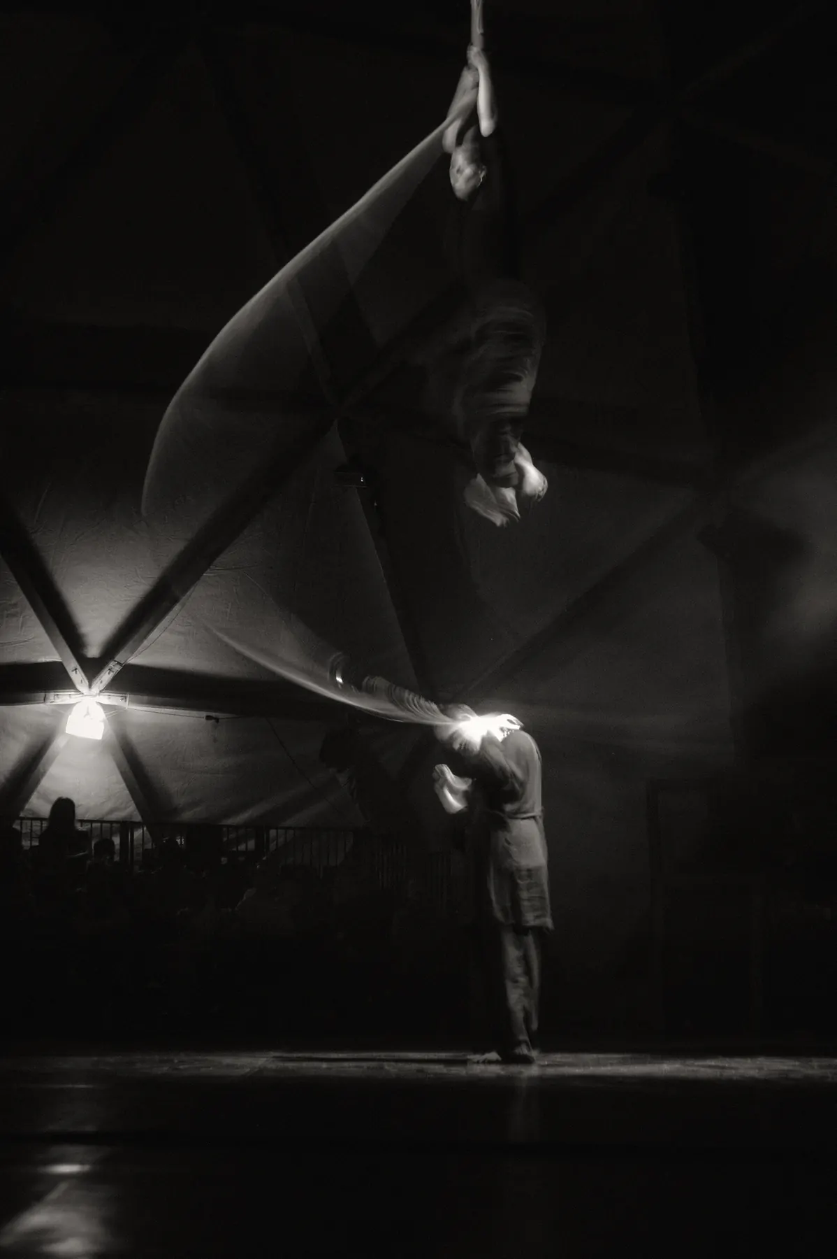The aerial silk billowing into a large wave in backlight, a person standing below in the beam