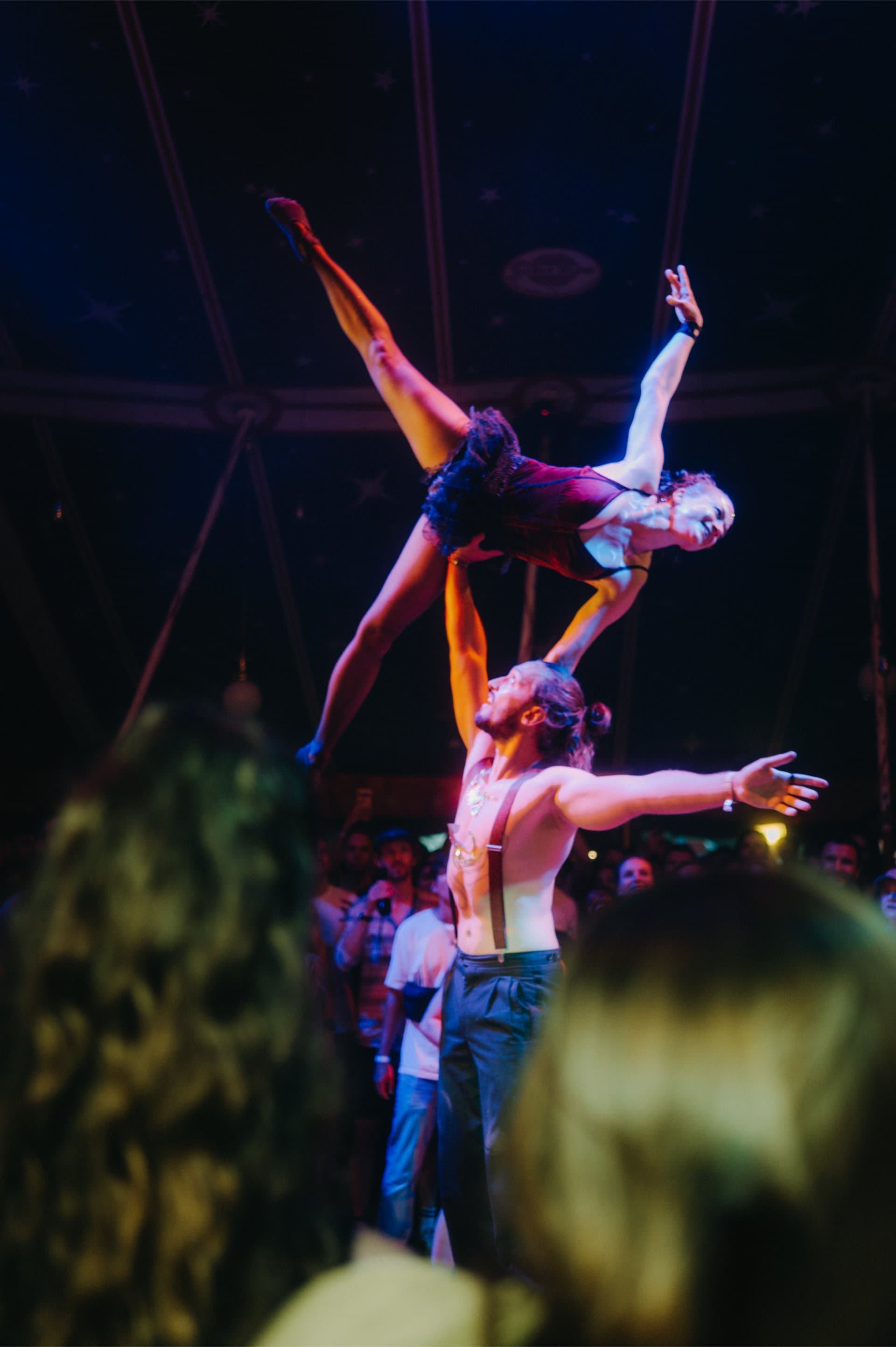 Three artists in a stacked acrobatic figure under the dome in coloured stage light, the audience in front