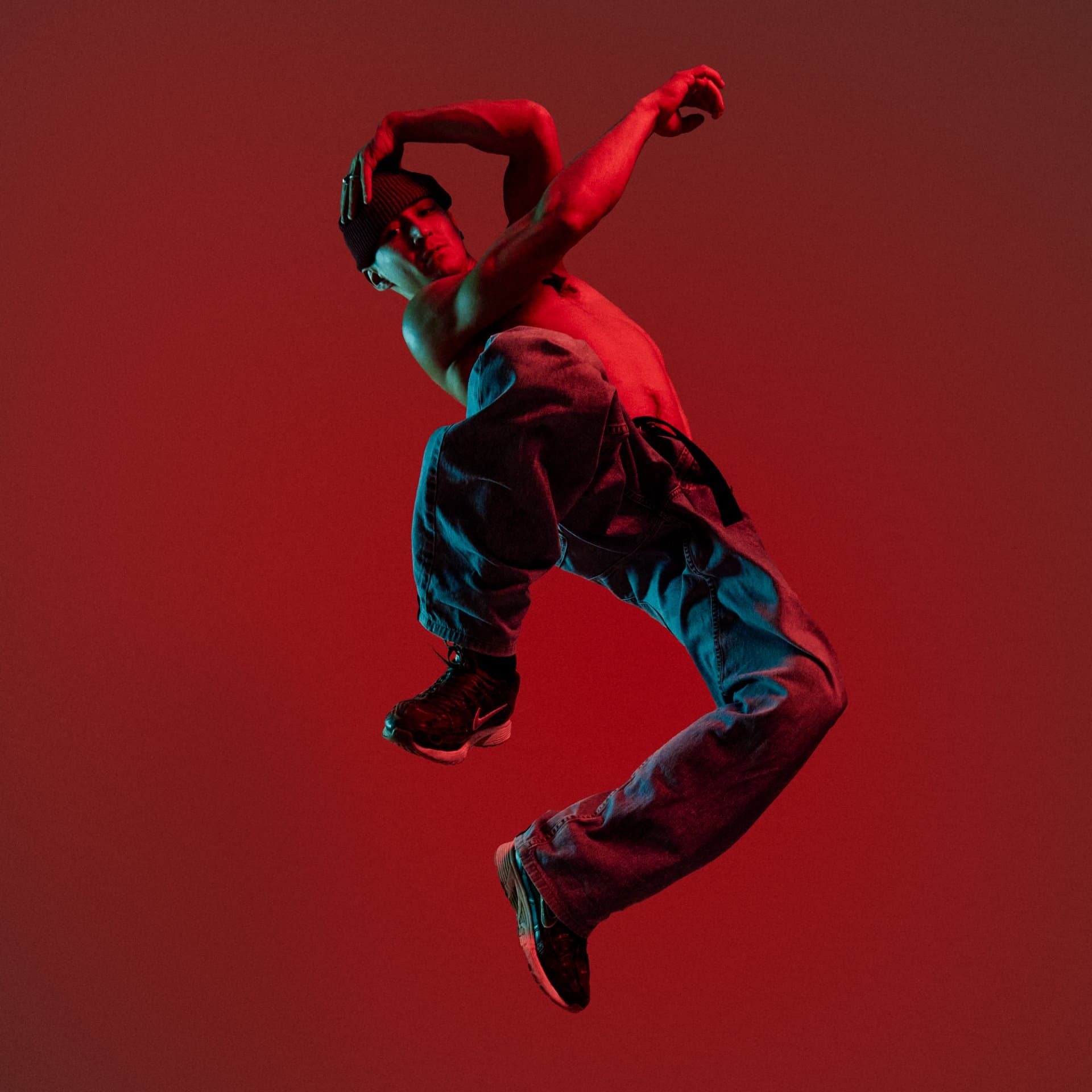 Artist mid jump against a red backdrop, the movement traced in red and turquoise light